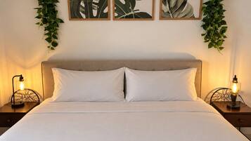 Een bed met witte beddengoed, twee bedlampen en drie ingelijste kunstwerken met bladeren aan de muur.