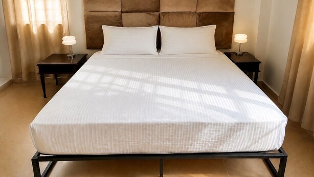 A hotel room with a large bed, two bedside tables, a headboard, and a window with curtains.