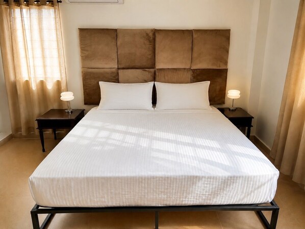 Habitación de hotel con una cama grande, dos mesitas de noche, un cabecero y una ventana con cortinas.