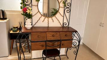 Une coiffeuse en bois avec un miroir, un petit tabouret et un vase rempli de fleurs.