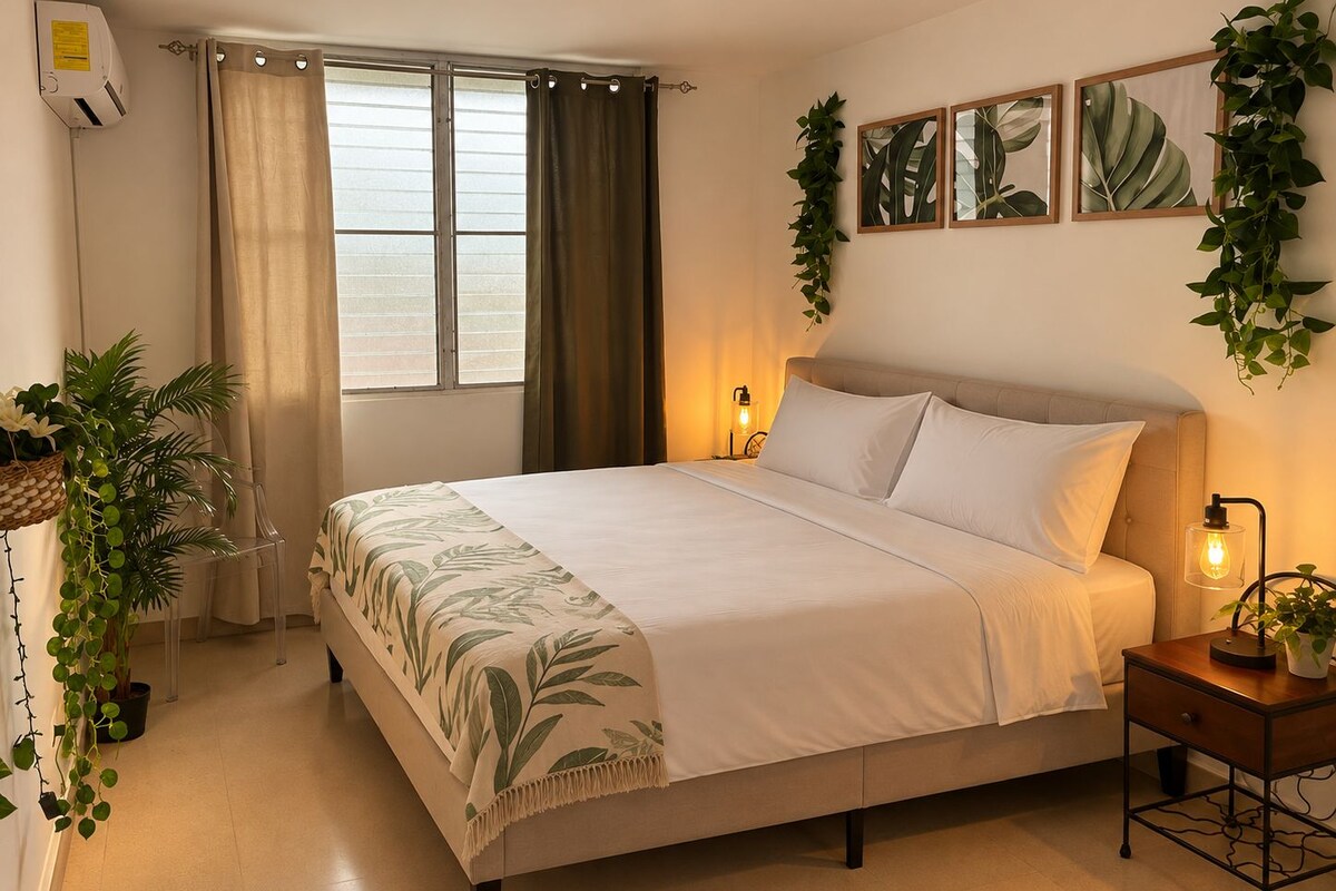 A bedroom with a bed, bedside table, wall-mounted plant, and a window with curtains.