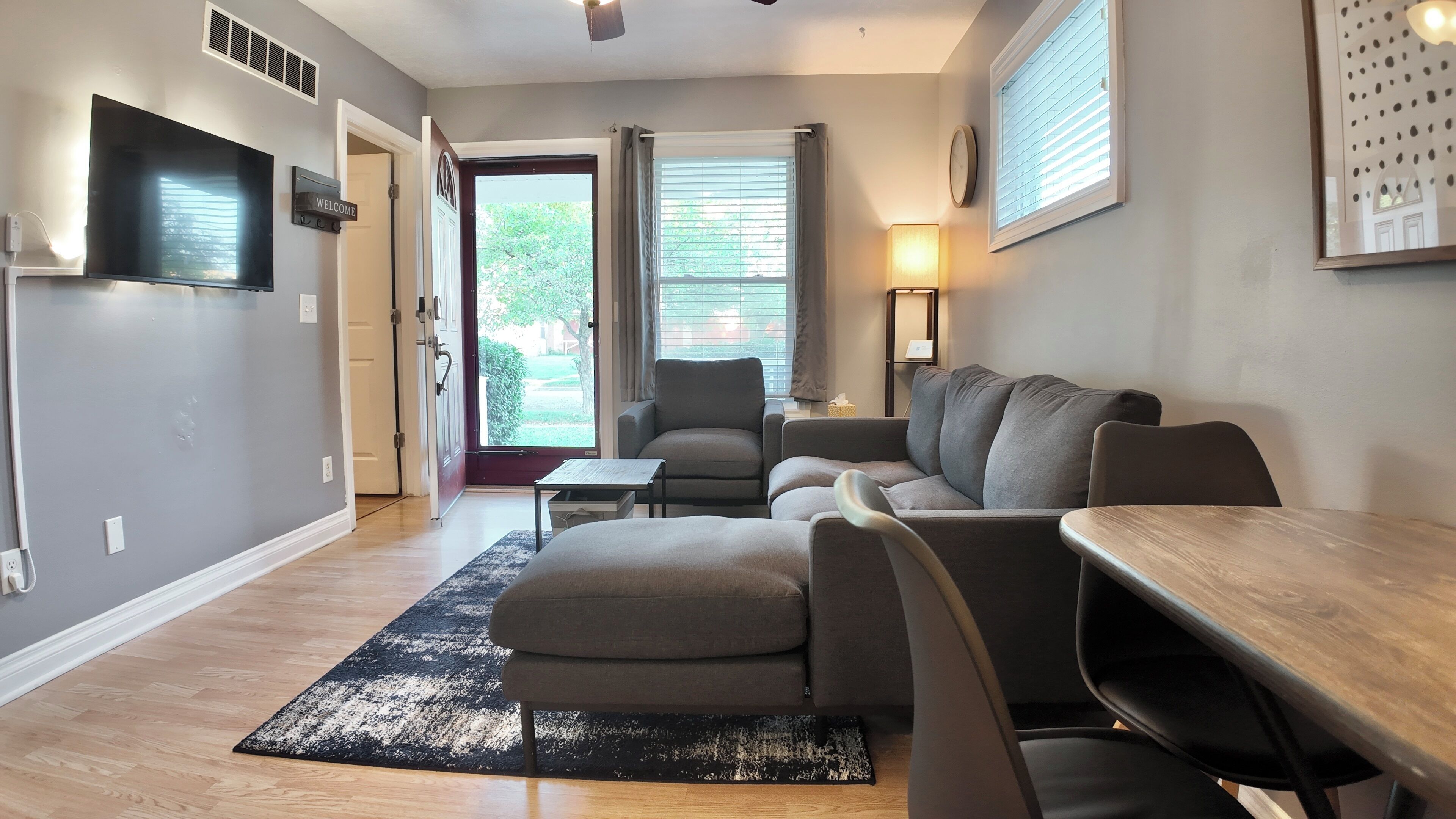 A modern living room with a sofa set, a dining table, and a TV mounted on the wall.