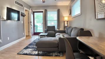 A modern living room with a sofa set, a dining table, and a TV mounted on the wall.