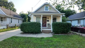 A single-story house with a front porch, two side hedges, and a car parked in the driveway. - The Comfort Street House - Pet-Friendly Home Near Downtown Lansing w/Office (Lansing)