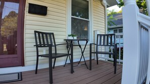 A porch with two chairs and a table, a window with blinds, and a small potted plant. - The Comfort Street House - Pet-Friendly Home Near Downtown Lansing w/Office (Lansing)