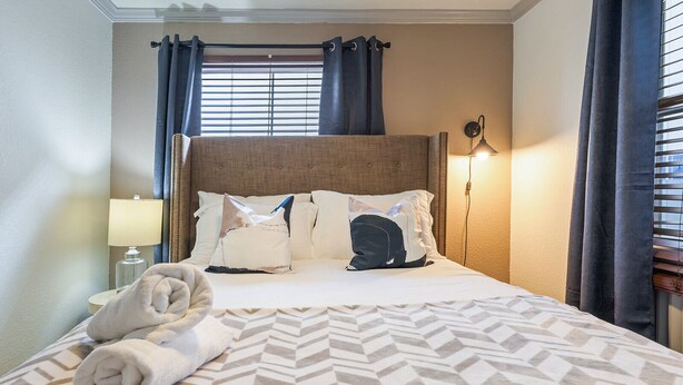 Une chambre d’hôtel avec un lit, une table de chevet avec une lampe et une fenêtre avec des rideaux.