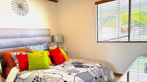 Quarto com cama, almofadas, luminária, janela e relógio de parede.
