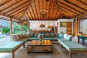 Ein geräumiges Wohnzimmer mit Holzbalkendecke, einem großen Sofa, einem Couchtisch und einem Essbereich.