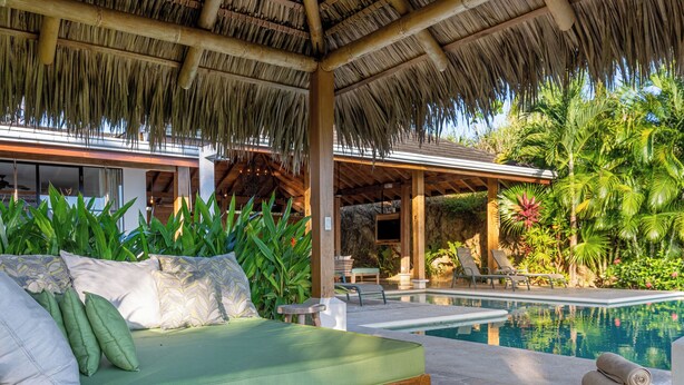 A poolside area with a green sofa, lounge chairs, and a thatched roof structure. - Casa la Onda "Ultra" Suite (Provincia de Puntarenas)