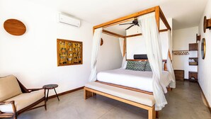 A four-poster bed with a ceiling fan, a wooden chair, a small round table, and a wall-mounted air conditioner. - Casa la Onda "Ultra" Suite (Provincia de Puntarenas)