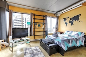 Ein modernes Schlafzimmer mit einem großen Bett, einem Fernseher, einer Weltkarte an der Wand und Blick auf Gebäude.
