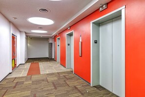 A hallway with carpeted flooring, red walls, and doors numbered 15. - Industrial-Style Cityscape 1 Bedroom Loft (Edmonton)