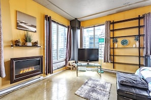 Ein Wohnzimmer mit Kamin, Fernseher, Sofa und großen Fenstern.