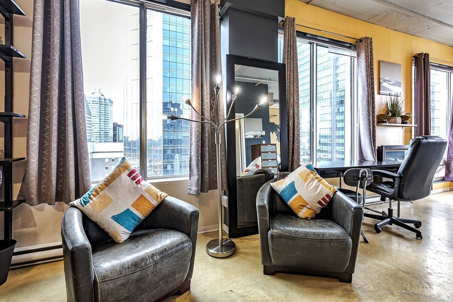 Un espace de bureau moderne comprenant deux fauteuils en cuir, un bureau et une grande fenêtre donnant sur la ville.