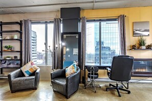 A modern living room with a city view, a fireplace, and a desk with a chair. - Industrial-Style Cityscape 1 Bedroom Loft (Edmonton)