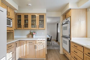 Una cocina con armarios de madera, microondas, refrigerador y comedor con mesa y sillas.