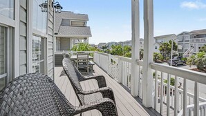 En takförsedd uteplats med möbler i rotting, ett bord och stolar, med utsikt över ett bostadsområde med hus och palmer.