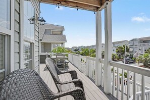 Eine überdachte Terrasse im Freien mit Korbmöbeln, einem Tisch und Stühlen, mit Blick auf eine Wohngegend mit Häusern und Palmen.