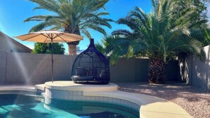 Ein Pool mit Vogelkäfig, Palmen und Sonnenschirm.