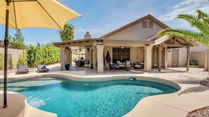 A pool with a curved edge, a covered patio area with outdoor furniture, and a building with a sloped roof. - Endless Summer Oasis by Avantstay Private Pool + Hot Tub + Putting Green Rooftop + Near Golf (Scottsdale)