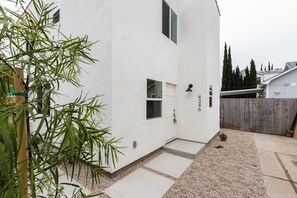 A white building with a small front porch, a door, and a window. There is a wooden fence in the background. - Spacious 4-bedroom townhome in delightful Los Angeles with AC (Los Angeles)