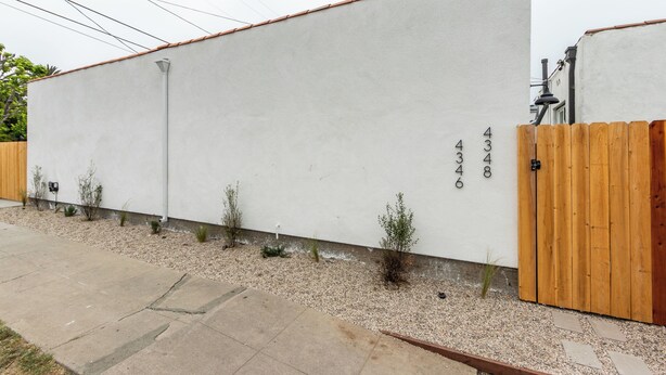 Een modern gebouw met een witte gevel, een houten hek en een grindpad.