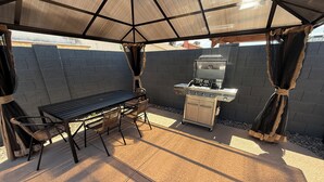 A covered outdoor patio with a grill, table, and chairs. - Beautiful 3-bedroom house with pool & game room in charming Glendale (Glendale)