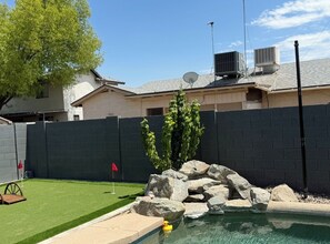A backyard with a swimming pool, artificial grass, a rock formation, and a fenced area. - Beautiful 3-bedroom house with pool & game room in charming Glendale (Glendale)