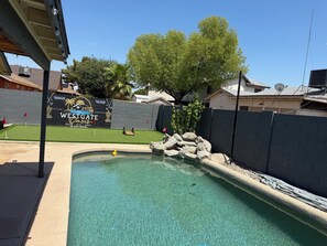 Ein Schwimmbecken mit Felsen, ein Schild mit der Aufschrift 'WESTGATE' und ein eingezäunter Garten mit Rasen und Bäumen.