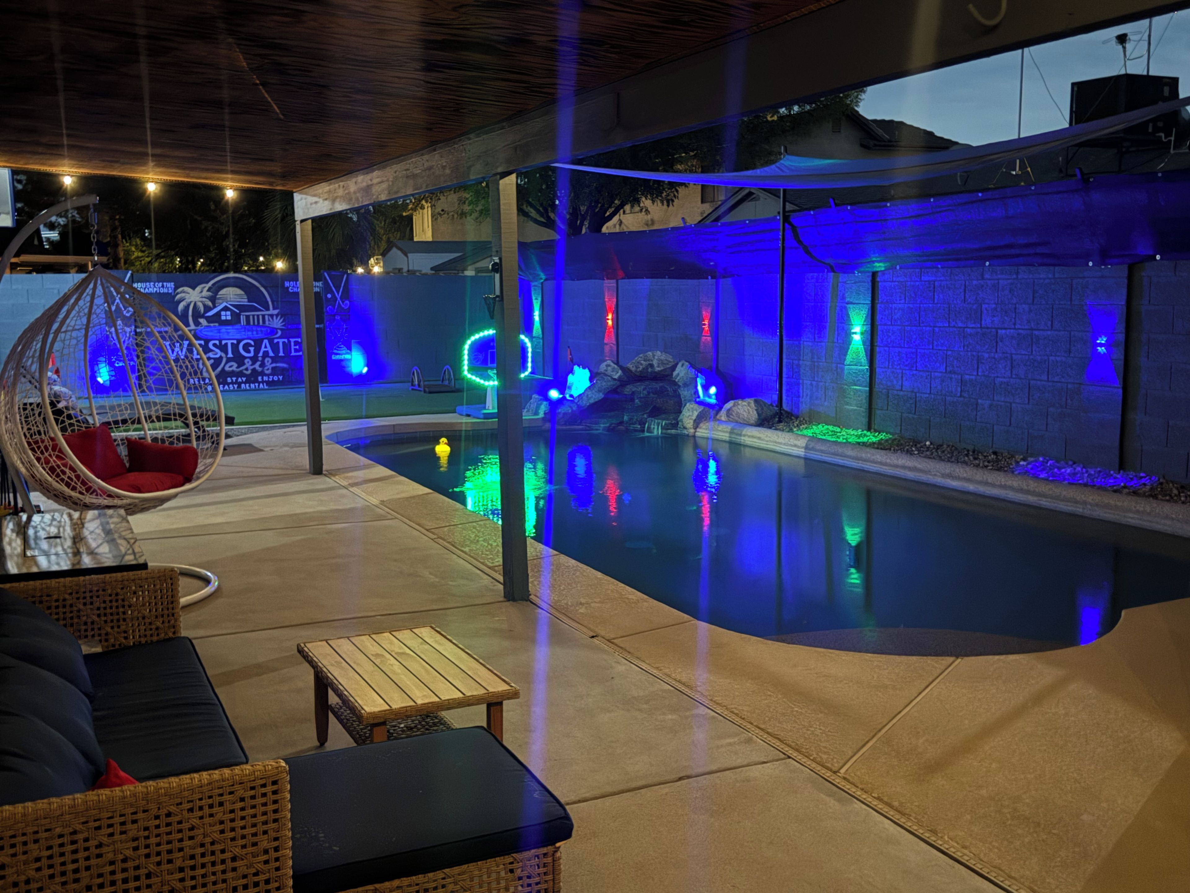 Un espace piscine extérieur comprenant un fauteuil suspendu, une table en bois et une chaise longue.
