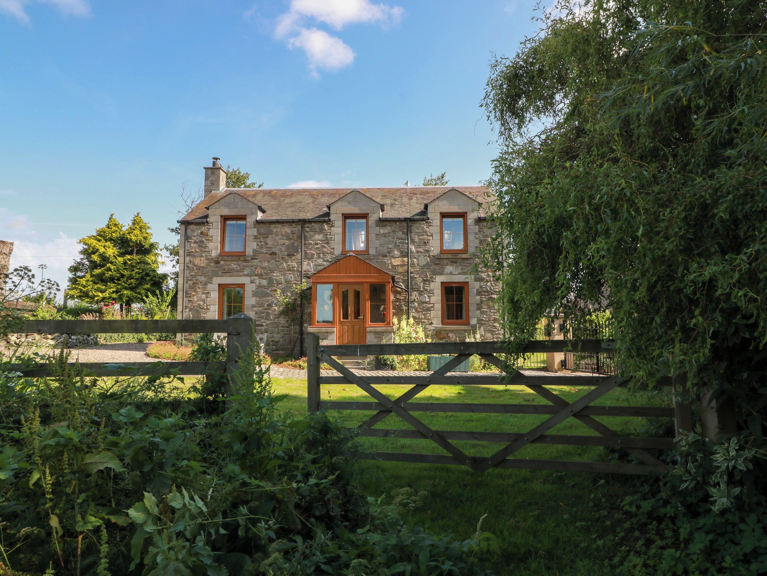 A stone house with a wooden front door, a fenced yard, and a clear sky.