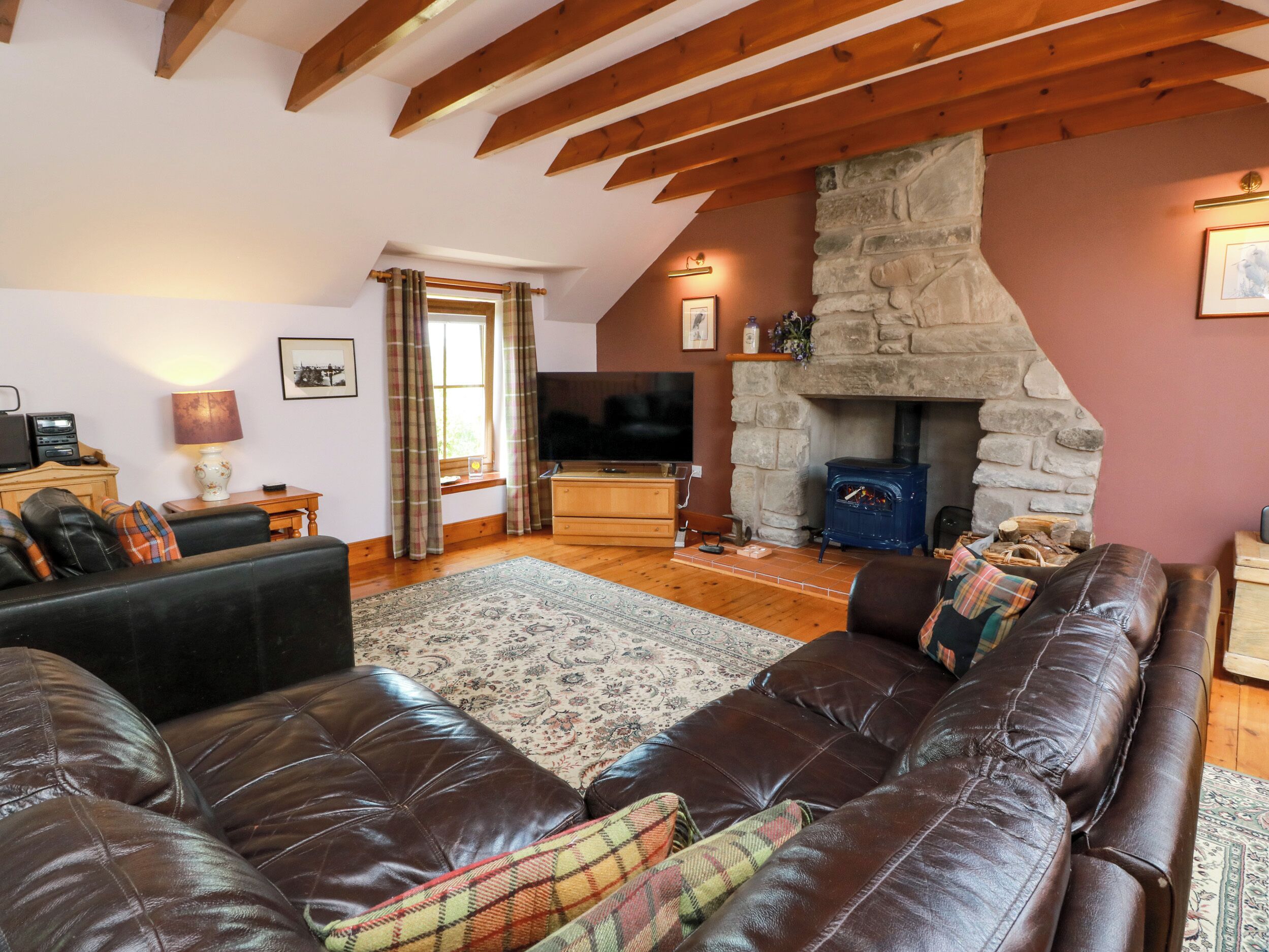 A cozy living room with a stone fireplace, leather sofas, a television, and a wooden ceiling.