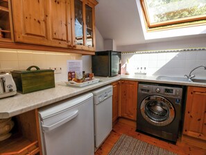 A kitchen with wooden cabinets, a dishwasher, a washing machine, a toaster, and a window with a view of trees.