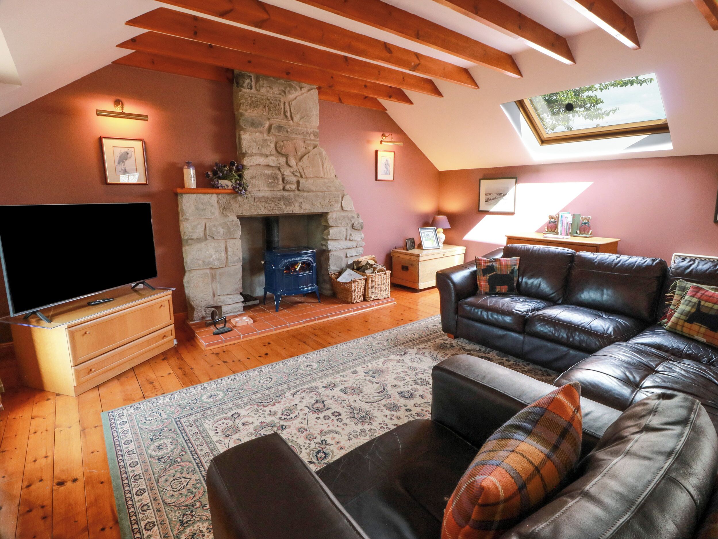 A cozy living room with a stone fireplace, a leather sofa, a flat-screen TV, and a skylight.