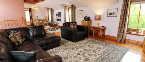 A living room with a brown leather sofa, a patterned rug, wooden flooring, and a dining area with a table and chairs.