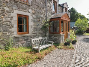 A stone building with a wooden bench, a small garden, and a cobblestone path. - Buchanans Bothy (Perth)