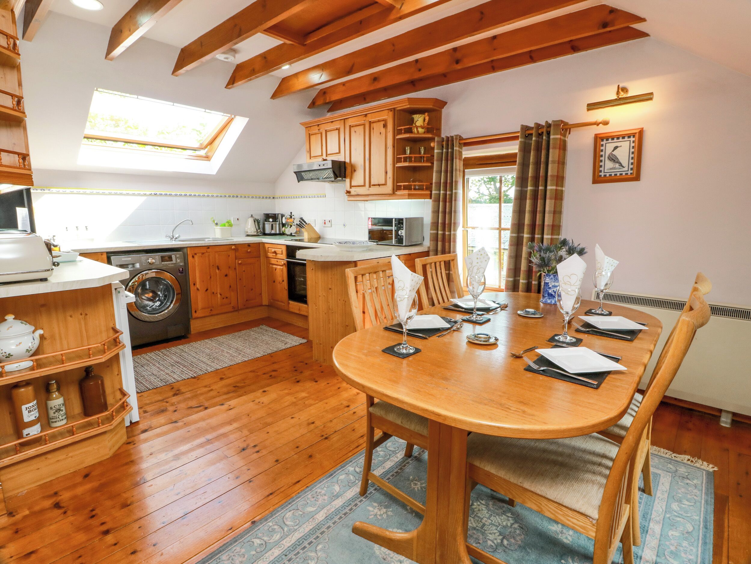 Une cuisine avec des meubles en bois, une table à manger pour quatre personnes et un lave-linge.