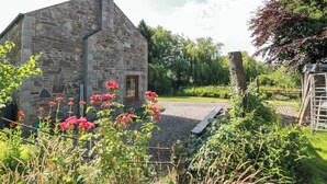 Un edificio de piedra con chimenea, rodeado de un jardín con flores rojas y un sendero de grava.