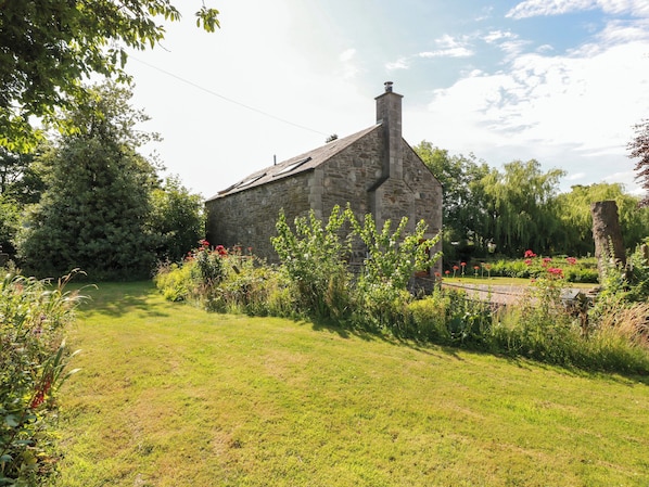 A stone building with a sloped roof, surrounded by a well-maintained garden with various plants and flowers.