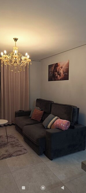 A living room with a dark brown sofa, a round coffee table, a chandelier, and a framed picture on the wall. - Beautiful apartment with ocean views on the Porto Seguro coastline, close to the best beaches. (Porto Seguro)