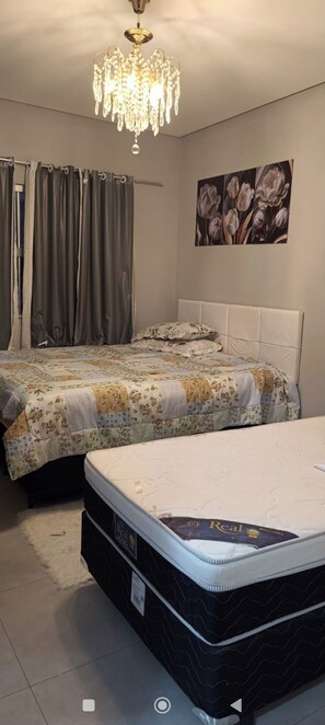 A bedroom with a queen-sized bed, a smaller bed, a chandelier, curtains, and a floral painting on the wall. - Beautiful apartment with ocean views on the Porto Seguro coastline, close to the best beaches. (Porto Seguro)