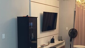 A modern living room with a flat-screen TV mounted on the wall, a dark wooden cabinet, a white console table, and a dining area with a marble table and chairs. - Beautiful apartment with ocean views on the Porto Seguro coastline, close to the best beaches. (Porto Seguro)