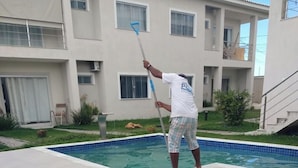 A person cleaning a swimming pool area with a long-handled tool. - Beautiful apartment with ocean views on the Porto Seguro coastline, close to the best beaches. (Porto Seguro)