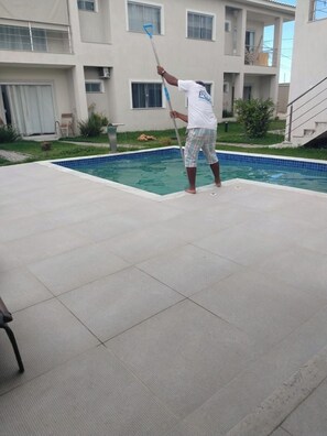 A person cleaning a swimming pool area with a long-handled tool. - Beautiful apartment with ocean views on the Porto Seguro coastline, close to the best beaches. (Porto Seguro)