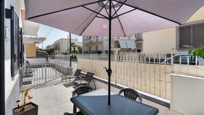 Ein Balkon mit Tisch und Stühlen, einem großen Sonnenschirm und Blick auf die Straße.
