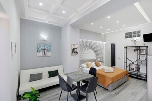 Una camera d'albergo moderna con un letto, una zona salotto con tavolo e sedie, un armadio e opere d'arte alle pareti.