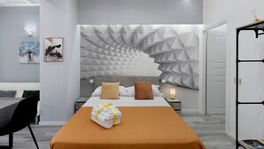 Une chambre à coucher moderne avec un motif géométrique sur le mur, un lit soigneusement fait et un coin repas avec une table et des chaises.