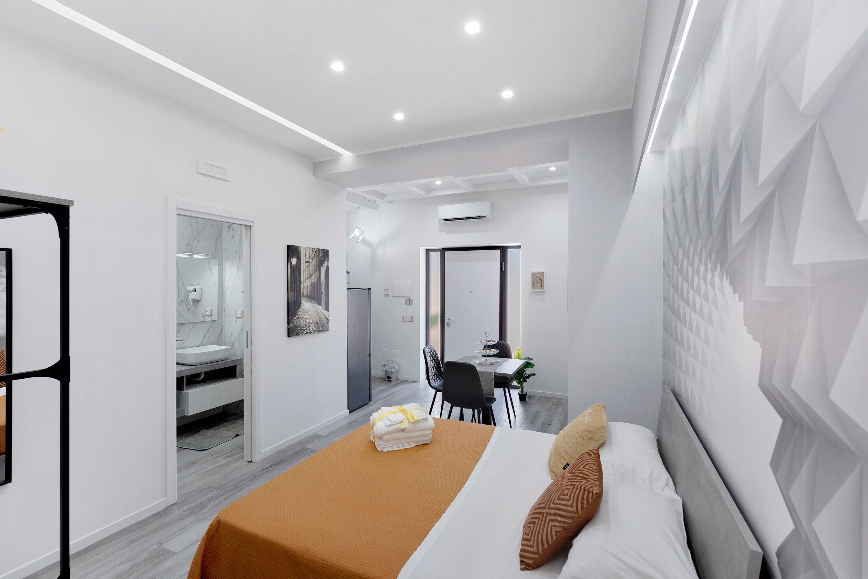 A modern hotel room with a bed, a dining area, and a bathroom.