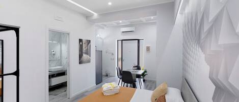 A modern hotel room with a bed, a dining area, and a bathroom.