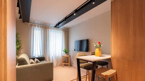 Ein modernes Wohnzimmer mit Sofa, Esstisch mit Stühlen, einem an der Wand befestigten Fernseher und einer Topfpflanze.